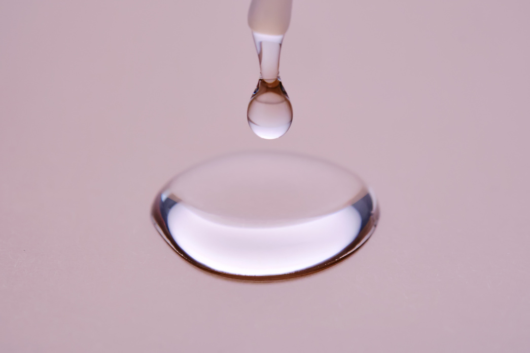 A drop of cosmetic product pours from a tube onto a pink background.